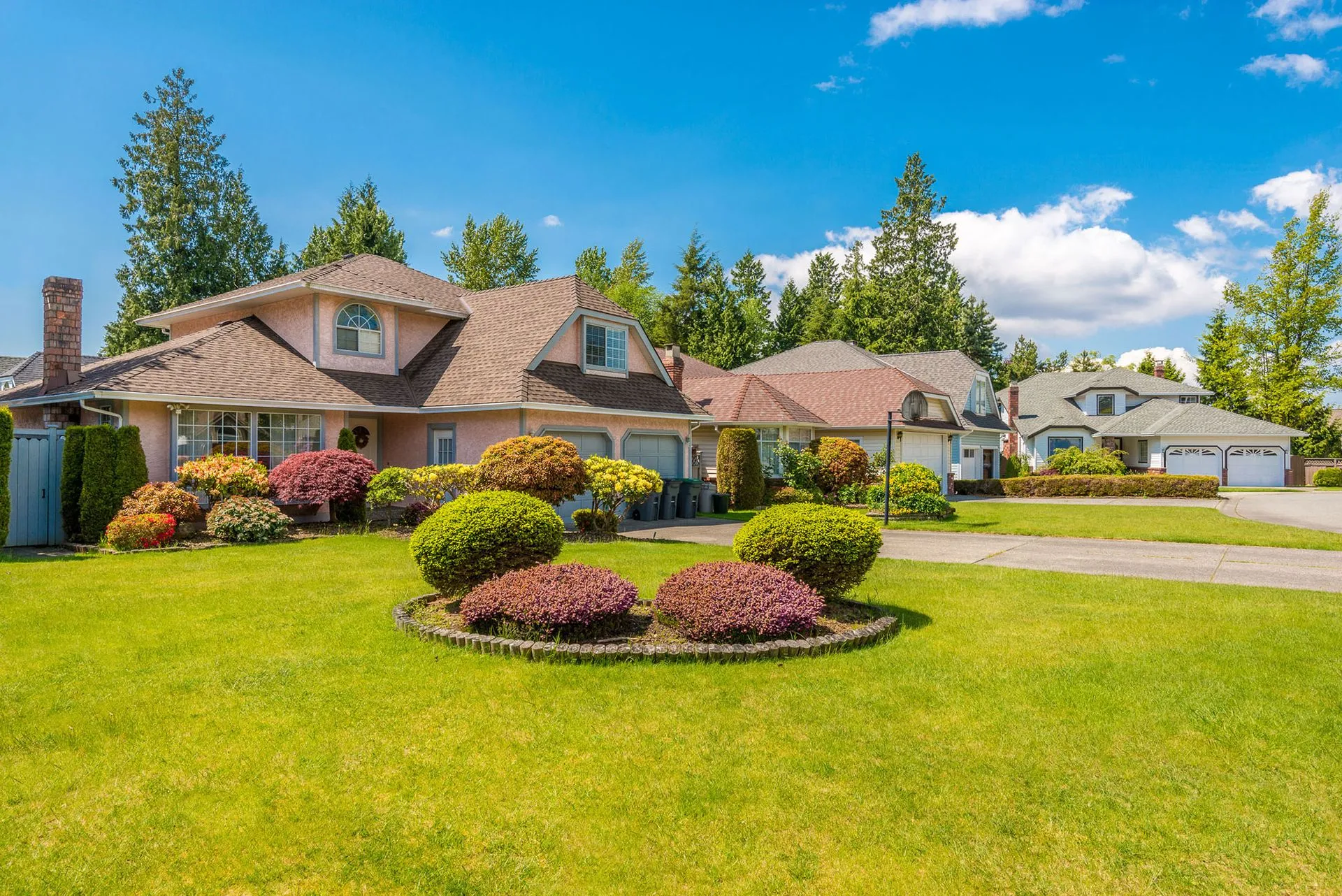 Well-maintained suburban front yard with lush green lawn, circular mulched shrub bed and trimmed ornamental bushes, landscaped flower beds and driveways in front of family homes — professional residential landscaping and hardscaping in Cedar Valley, Iowa
